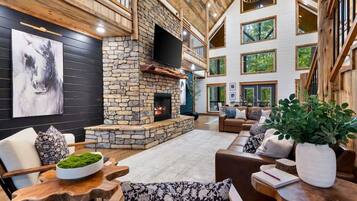 Un espacio habitable espacioso con chimenea de piedra, techo de madera y ventanas grandes.