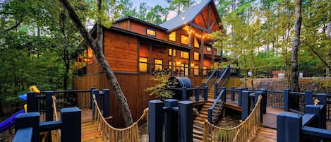 A wooden cabin with a deck, surrounded by trees.