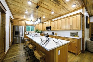 A modern kitchen with wooden cabinets, stainless steel appliances, and a marble island with bar stools.