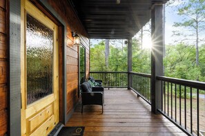 A wooden porch with a railing, a door with a glass panel, and a bench. - 6 Bed, 4.5 Bath, Pool, Sauna, Hot Tub, Games, Pets (Broken Bow)