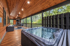 A wooden deck with a hot tub, outdoor seating, and a stone fireplace.