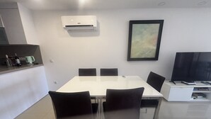 Zona pranzo moderna con tavolo bianco, quattro sedie, angolo cottura con macchina del caffè e condizionatore d'aria a parete.