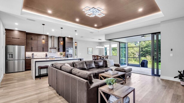 A modern kitchen with a built-in oven and refrigerator, a dining area with a large table, and a living room with a sectional sofa and a coffee table. - Brand New, Family Friendly Spacious- Home Sleeps 12 + 10 mins to Gulf Beaches (Englewood)