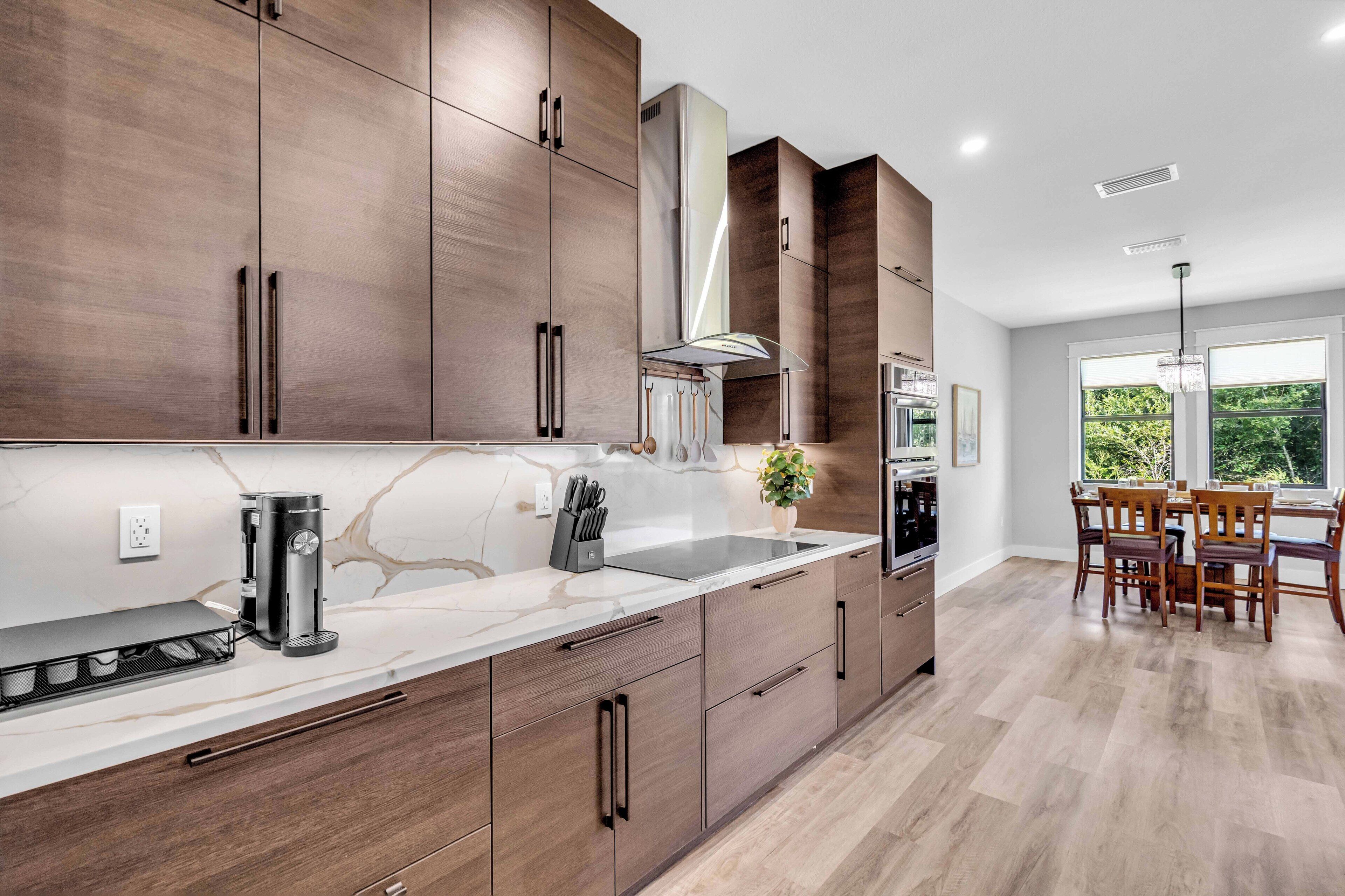 A modern kitchen with wooden cabinets, a marble countertop, and a dining area with wooden chairs.
