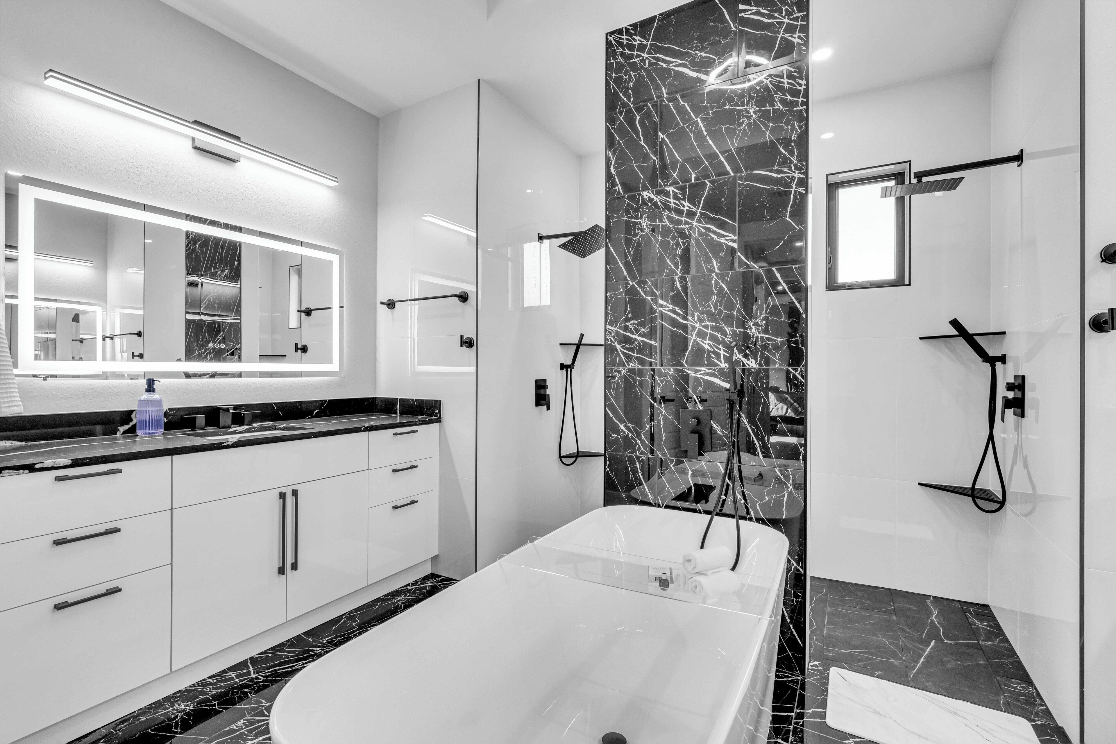 Un baño moderno con un espejo grande, una bañera y paredes de mármol.