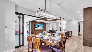 A modern dining area with a wooden table set for four, surrounded by chairs with cushioned seats. - Brand New, Family Friendly Spacious- Home Sleeps 12 + 10 mins to Gulf Beaches (Englewood)