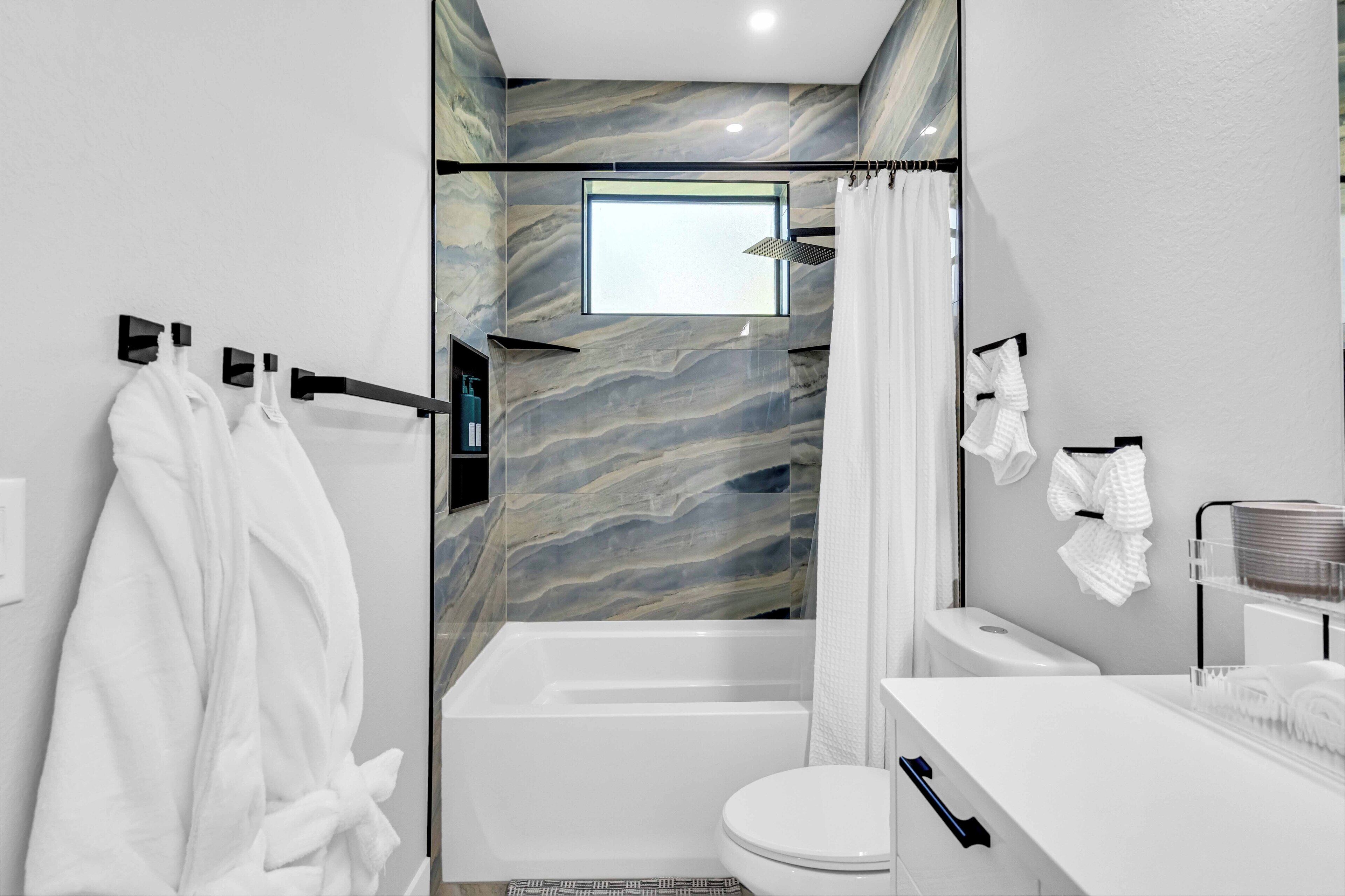 Un baño moderno con pared de mármol, bañera, inodoro y lavabo con toallero.
