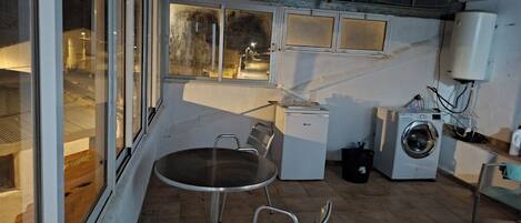 A compact kitchen with a small table and chairs, a washing machine, and a window overlooking a street.