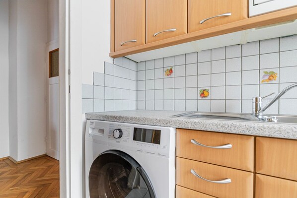 A compact kitchen with a washing machine, wooden cabinets, and a tiled backsplash.