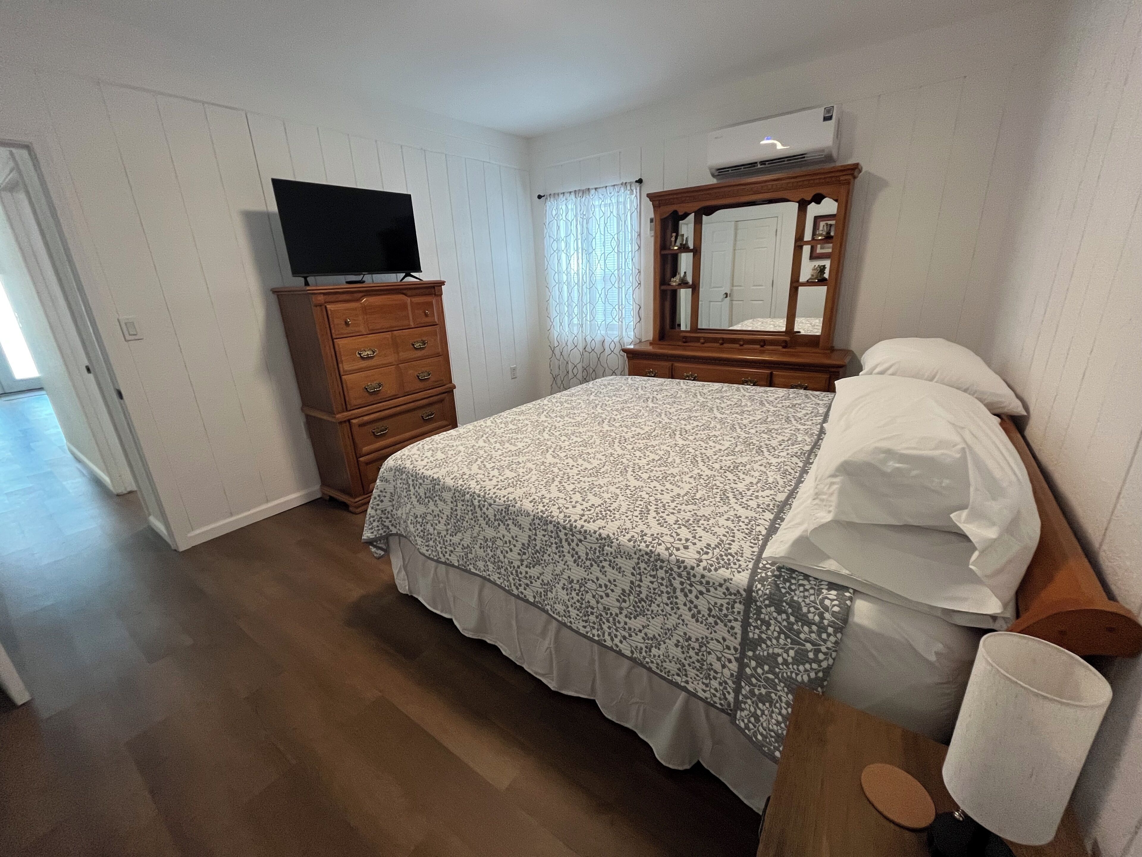 Une chambre à coucher avec un lit, une commode, une télévision et un miroir.