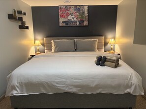 Ein ordentlich bezogenes Bett mit weißen Laken, zwei Nachttische mit Lampen und ein motivierender Poster an der Wand.