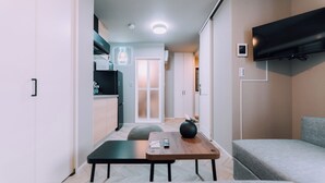 A modern living room with a flat-screen TV mounted on the wall, a wooden table with a vase, and a grey sofa. - Showa Bloom · Cozy Stay Near Shinjuku (Tokyo)