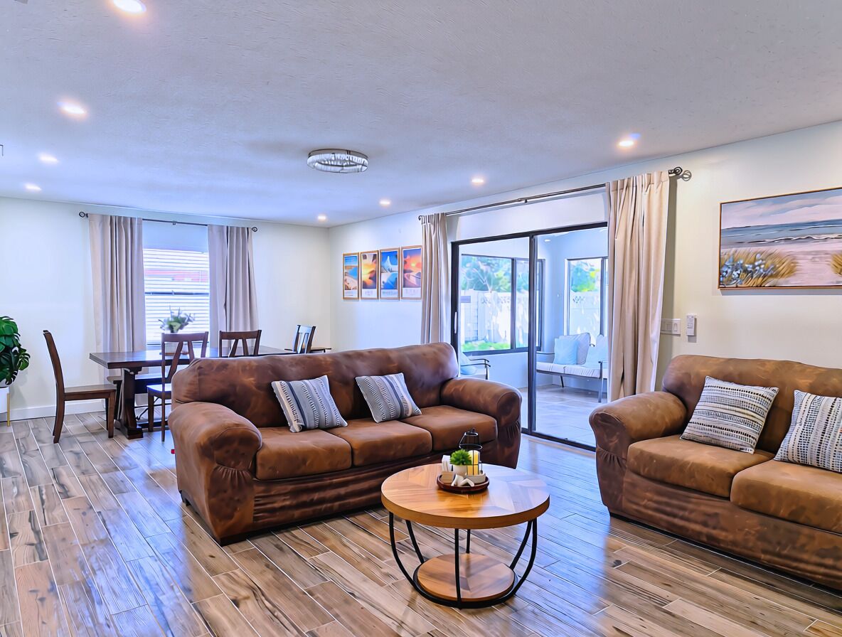 A modern living room with two brown leather sofas, a wooden coffee table, and a dining area with a table and chairs.