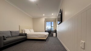 A hotel room with a bed, a sofa, a desk, and a TV mounted on the wall. - Harbour View Lodge (Porirua)