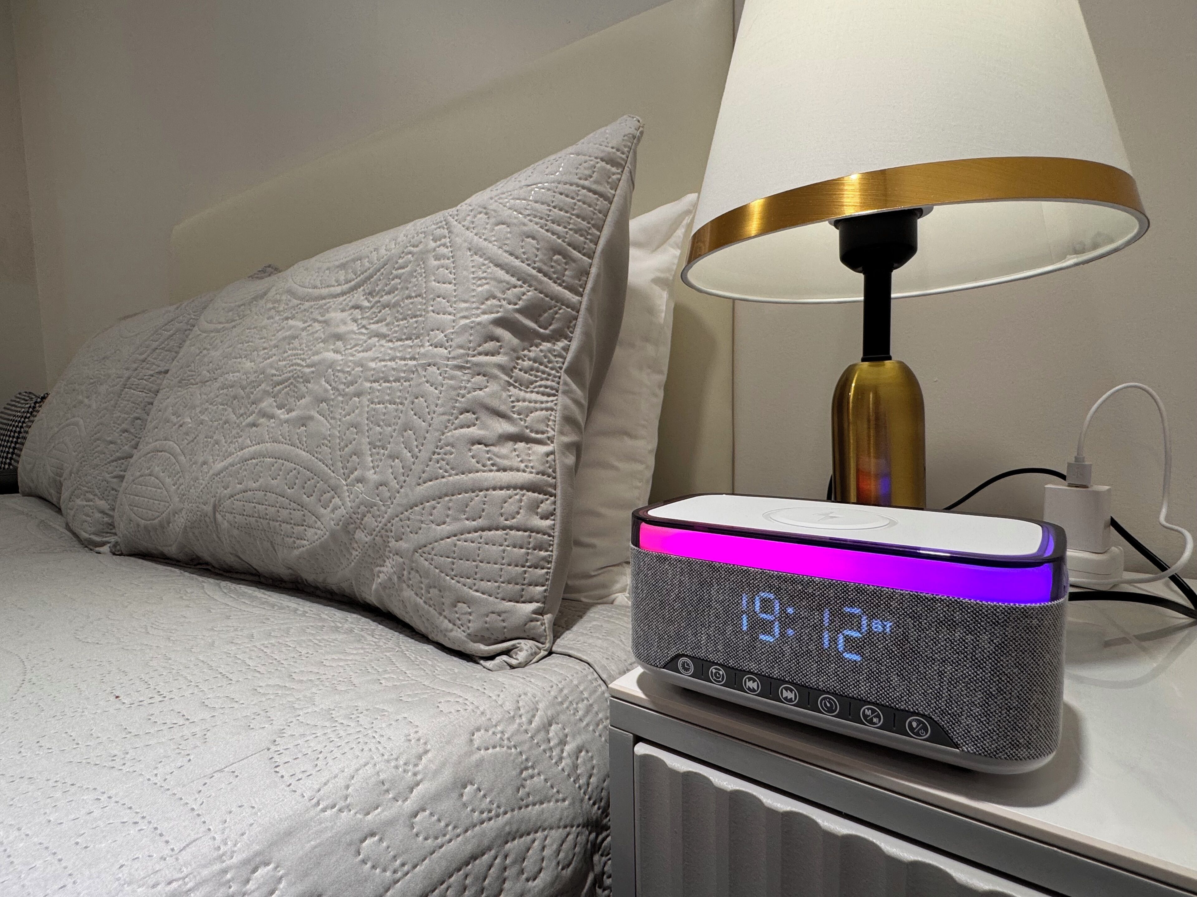 A bedside table with a digital clock displaying the time, a lamp, and a pillow.