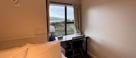 A hotel room with a bed, a desk with a chair, a telephone, and a window with curtains.
