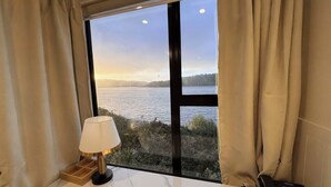 A room with a large window overlooking a body of water, a lamp on a marble table, and a telephone on the right side. - Harbour View Lodge (Porirua)
