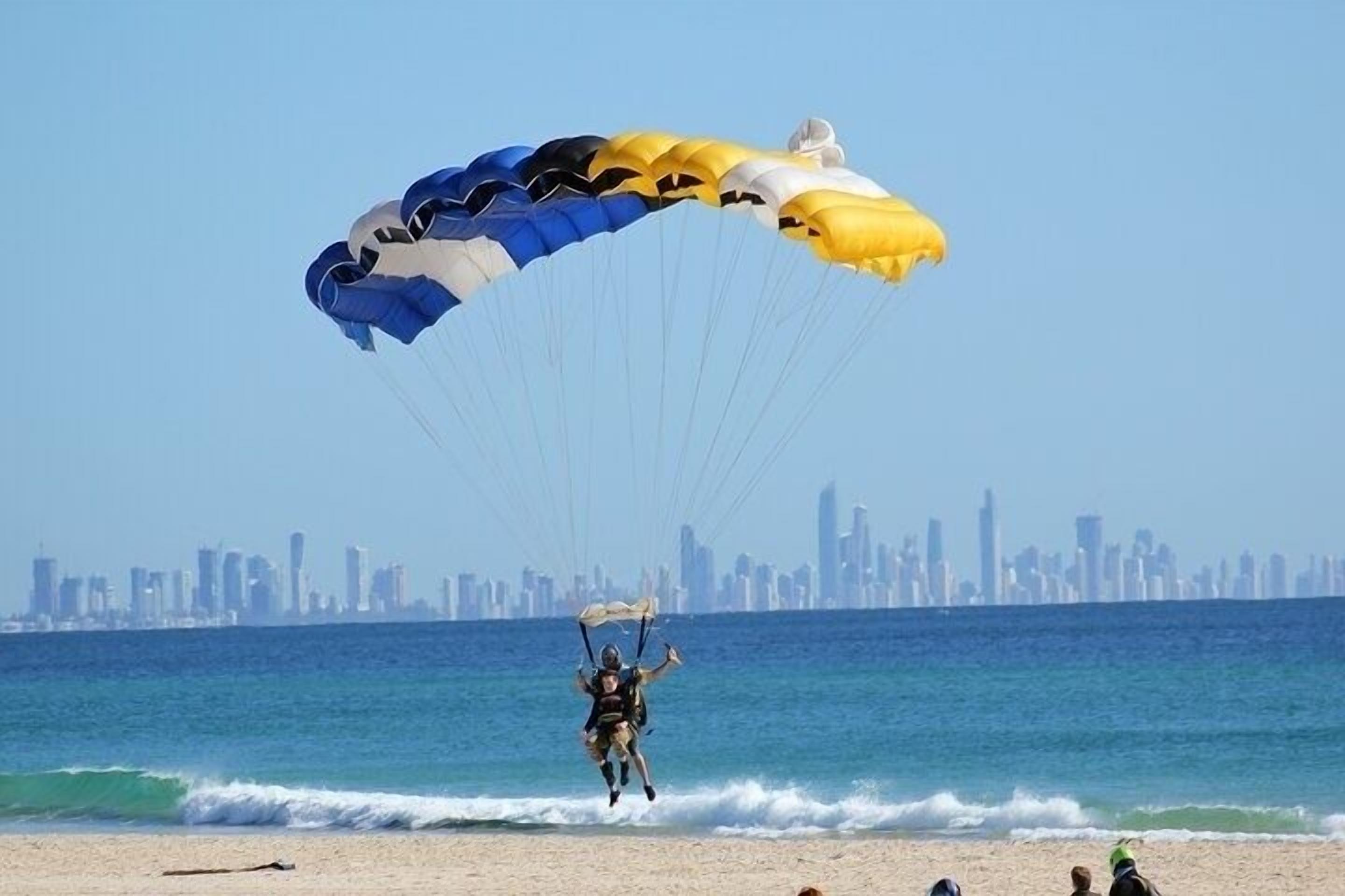 A person parachuting into a beach area with a city skyline in the background.