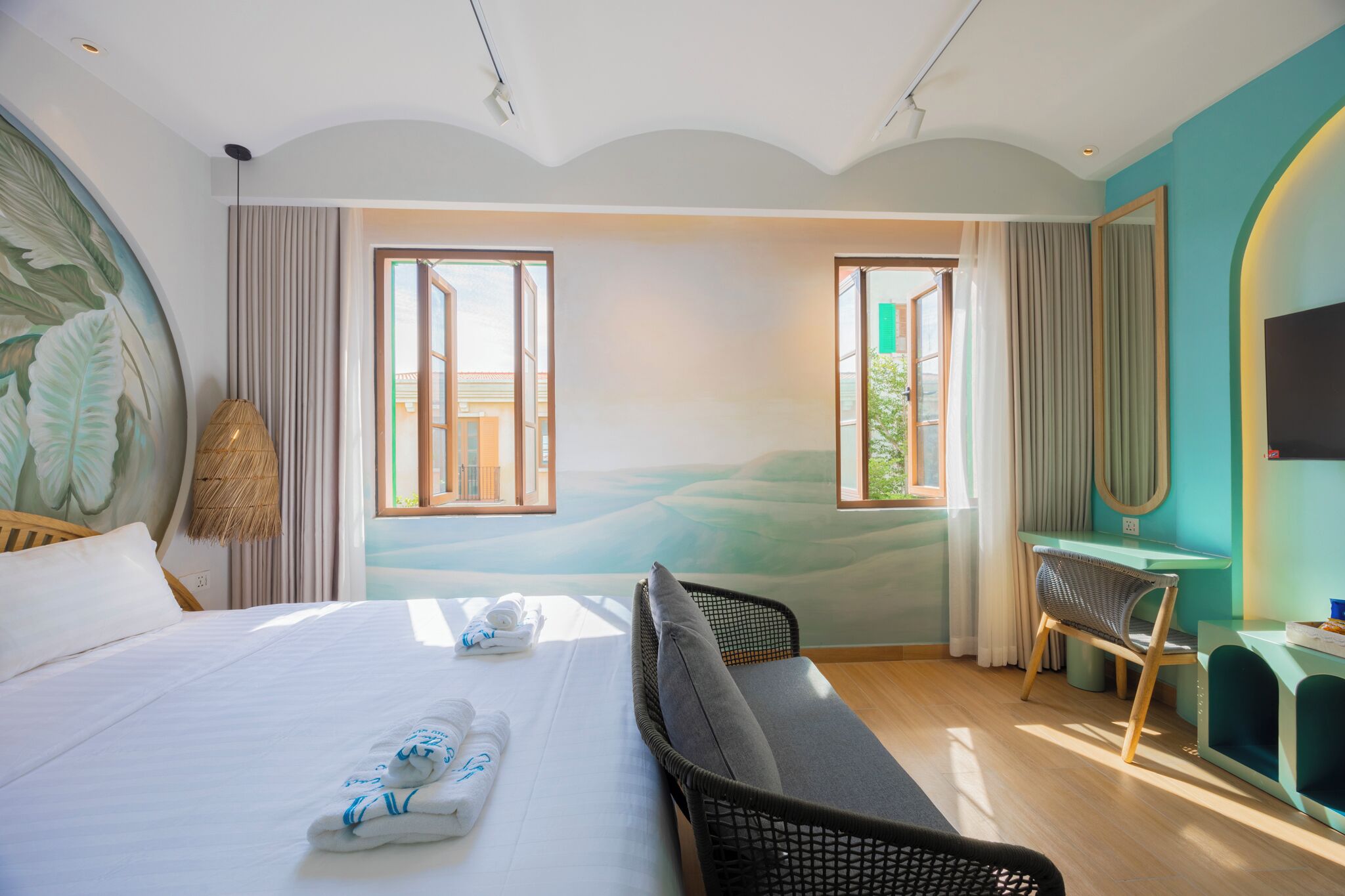 A modern hotel room with a large bed, a desk, and a view of a green landscape through the windows.