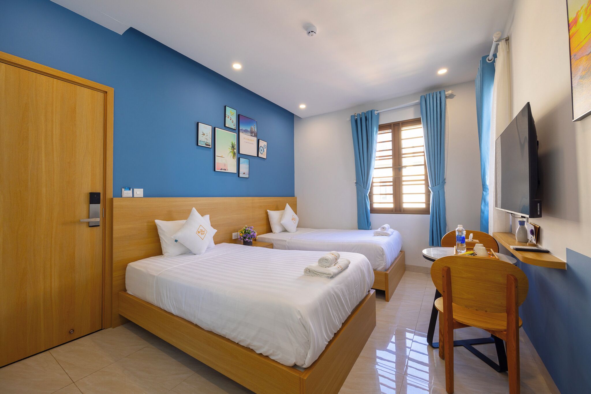 Une chambre d’hôtel avec deux lits, un bureau, une chaise, une télévision et une fenêtre avec des rideaux.