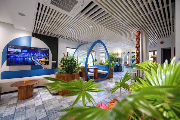 A modern hotel lobby with a large flat-screen TV, seating areas, and potted plants. - Lotus Home Cafe – Budget (Phu Quoc)