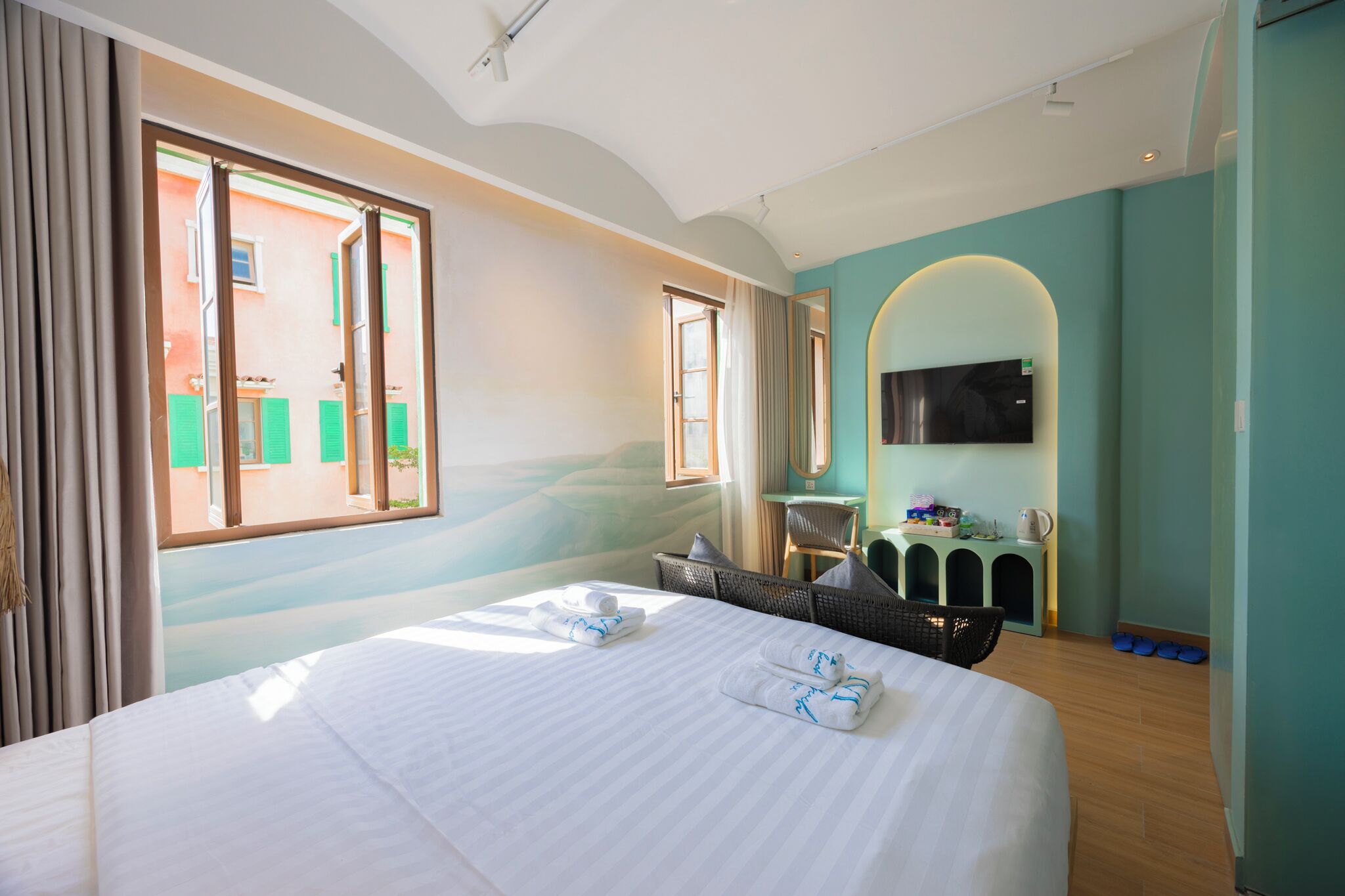 Quarto de hotel com uma cama grande, uma televisão, uma escrivaninha pequena e vista para um edifício.