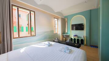 Quarto de hotel com uma cama grande, uma televisão, uma escrivaninha pequena e vista para um edifício.