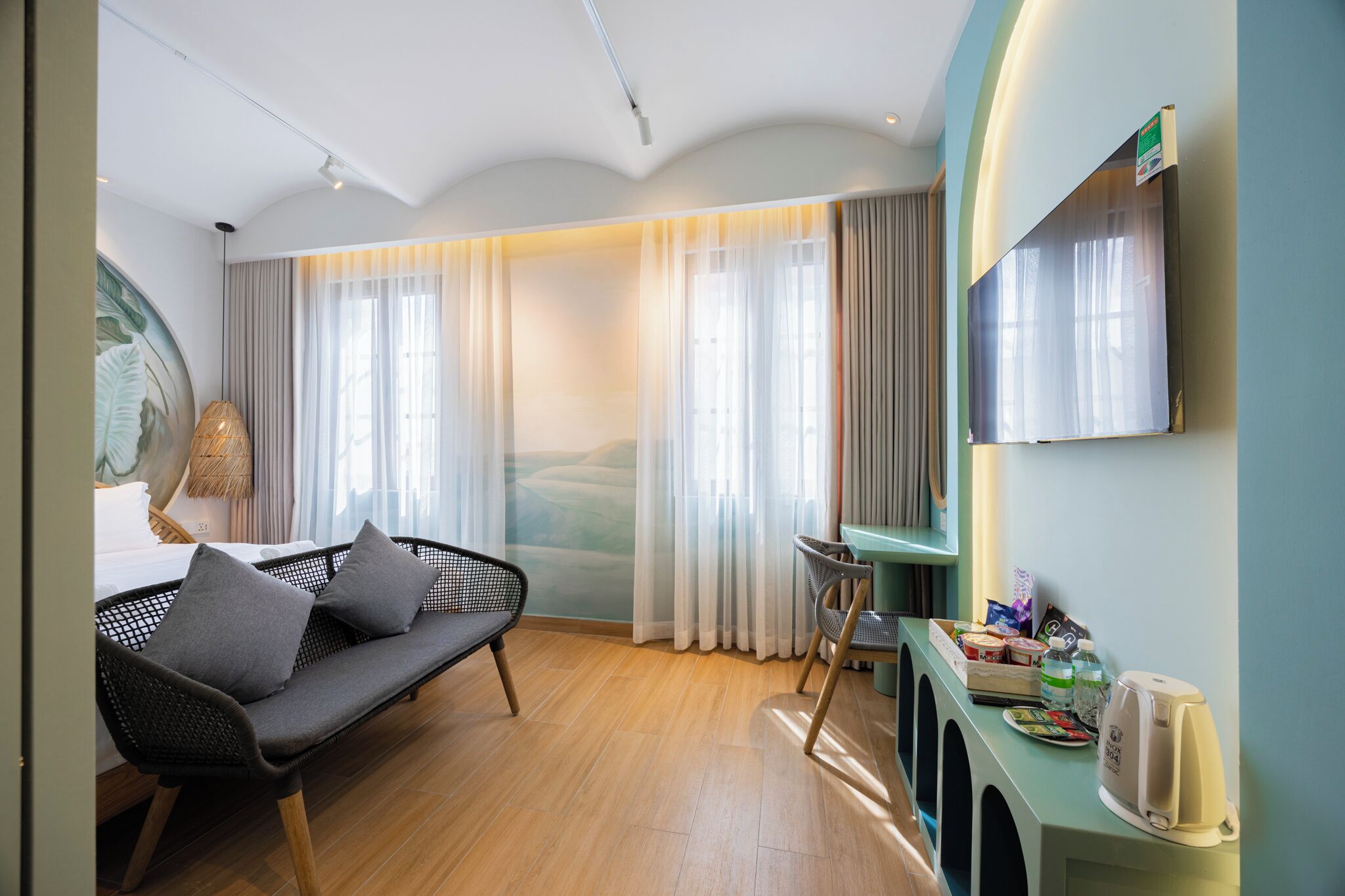 A modern hotel room with a sofa, dining table, and a TV mounted on the wall.