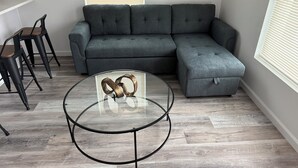 Un salon moderne avec un canapé d’angle gris, une table basse en verre avec un cadre en métal et un plancher en bois.