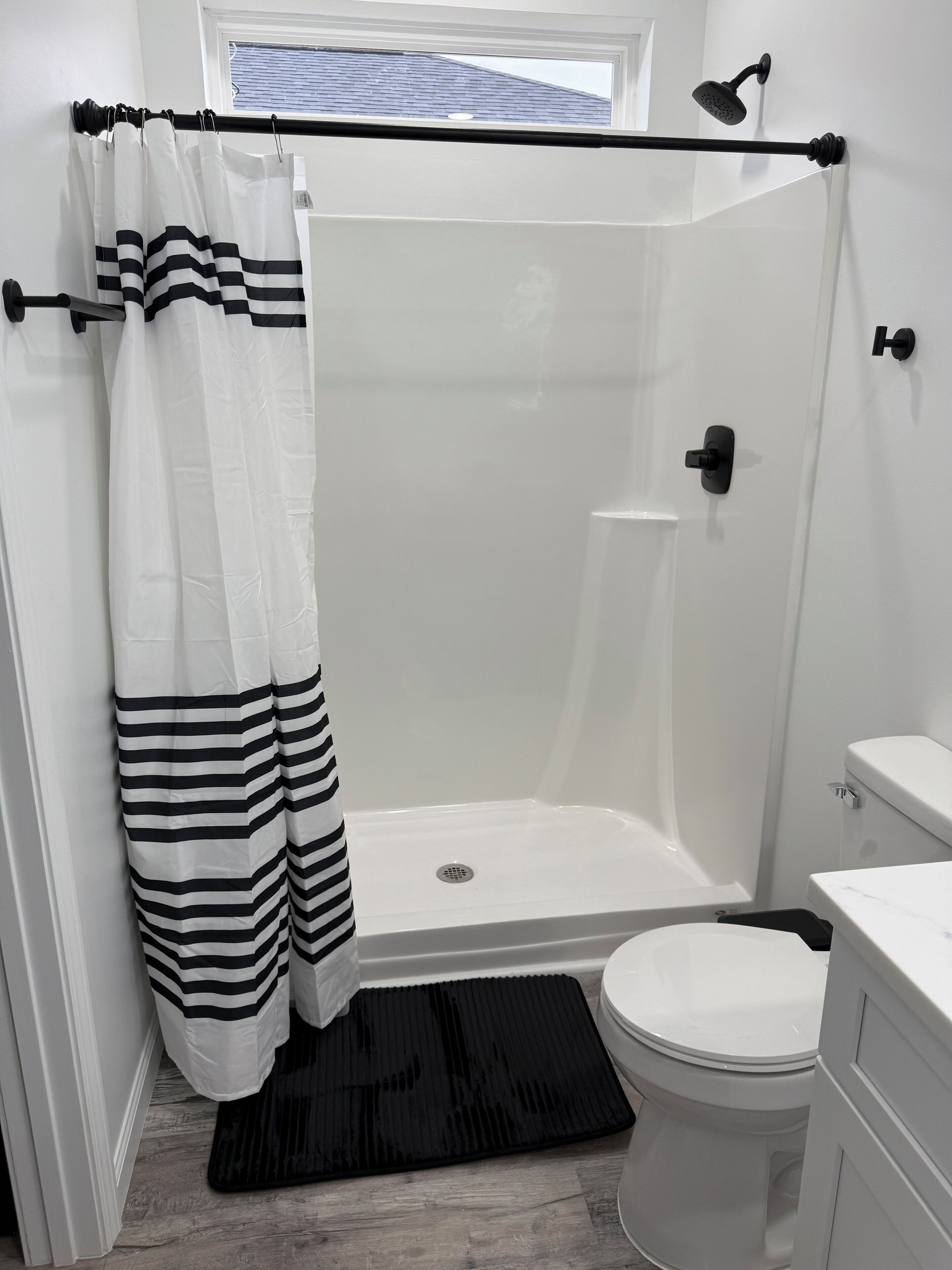 Ein modernes Badezimmer mit einer gläsernen Duschkabine, einer weißen Toilette und einem schwarzen Duschvorhang.
