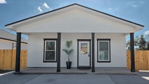 Une maison de plain-pied avec un toit à pignon, une véranda à l’avant dotée de colonnes noires et une petite plante en pot.