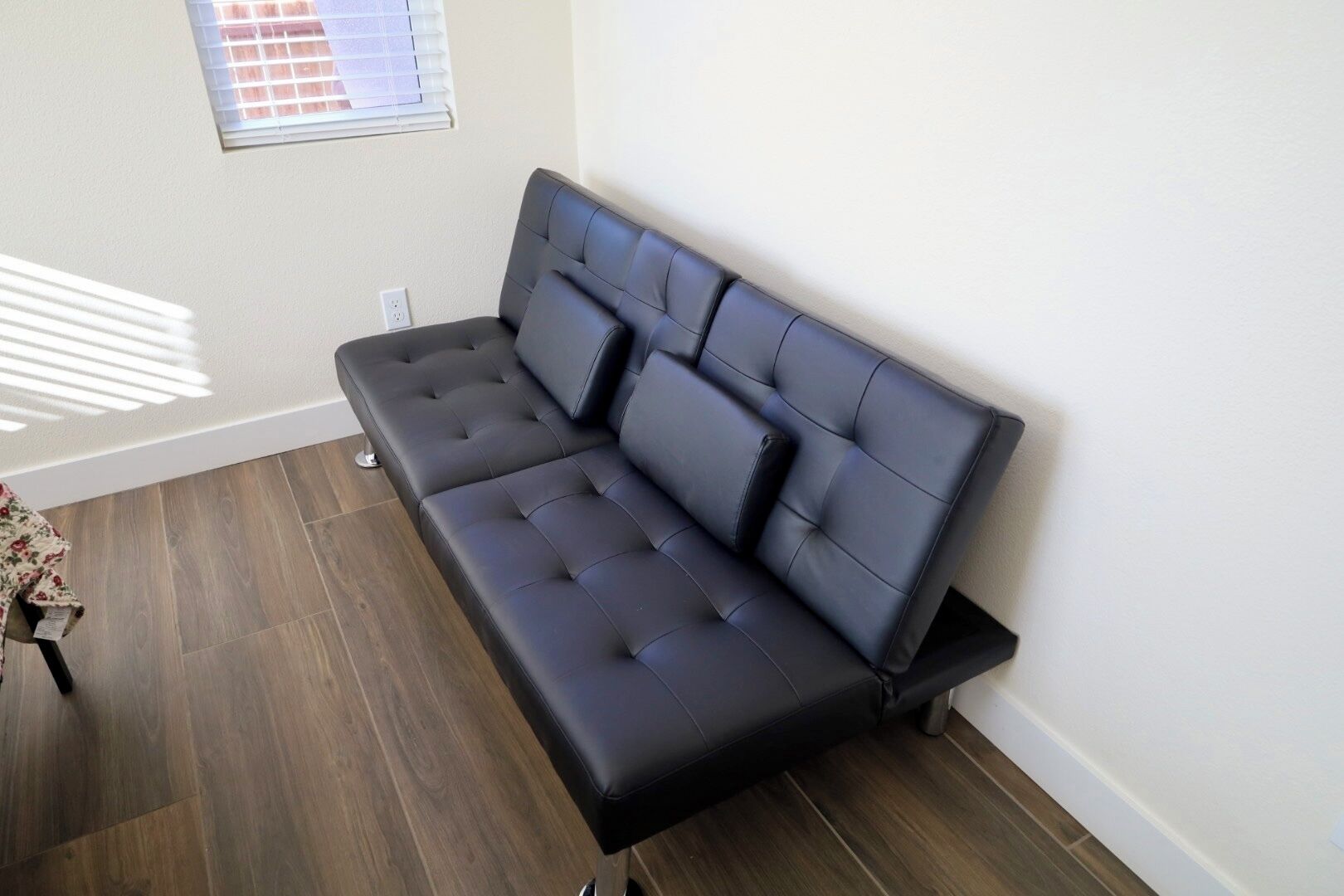 Een moderne woonkamer met een donker leren bank, houten vloeren en een raam met zonwering.