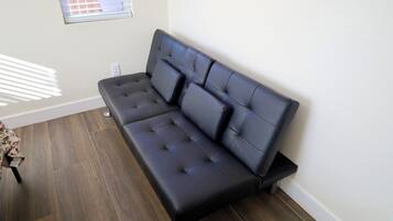 Een moderne woonkamer met een donker leren bank, houten vloeren en een raam met zonwering.