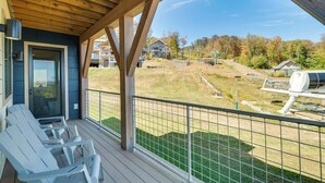 A covered outdoor area with a wooden deck, a glass door, and a view of a residential area with houses and trees. - Ski-In Out on Okemo, 25 minutes to Killington, 8 minutes to Fox Run Golf Club! (Ludlow)