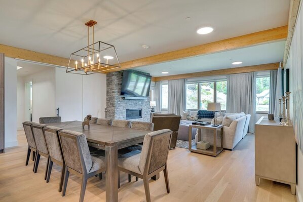 Un amplio salón con una gran mesa de madera para comer, asientos cómodos, una chimenea de piedra y un televisor.