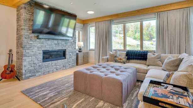 A living room with a stone fireplace, a large window with curtains, a beige sofa, and a wooden ceiling. - Ski-In Out on Okemo, 25 minutes to Killington, 8 minutes to Fox Run Golf Club! (Ludlow)