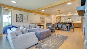 A modern living room with a grey sofa, a dining area with a wooden table and chairs, and a kitchen with white cabinets and a stainless steel range hood. - Ski-In Out on Okemo, 25 minutes to Killington, 8 minutes to Fox Run Golf Club! (Ludlow)
