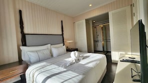 A hotel room with a large bed, a wooden headboard, a bedside table, a desk with a computer, and a shower area visible through an open door. - GrandFlorida 1Bedroom CloseToBeach D716 (Sattahip)