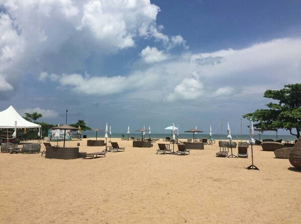 Une plage avec des chaises longues, des parasols et une tente blanche.