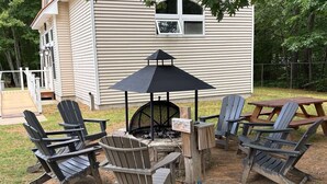 An outdoor seating area with Adirondack chairs and a table, surrounded by a stone fire pit and a black umbrella. - Attitash Townhouse: 1BR w/AC, Pool, Storyland (Bartlett)