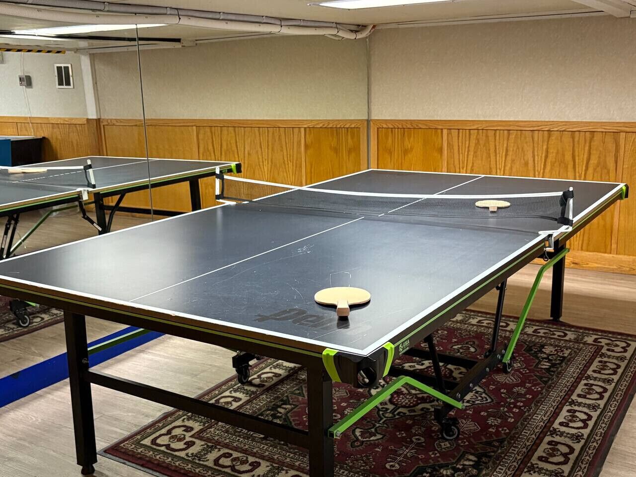 Ein Zimmer mit Pongtischen, einem gemusterten Teppich und Holzvertäfelung an den Wänden.