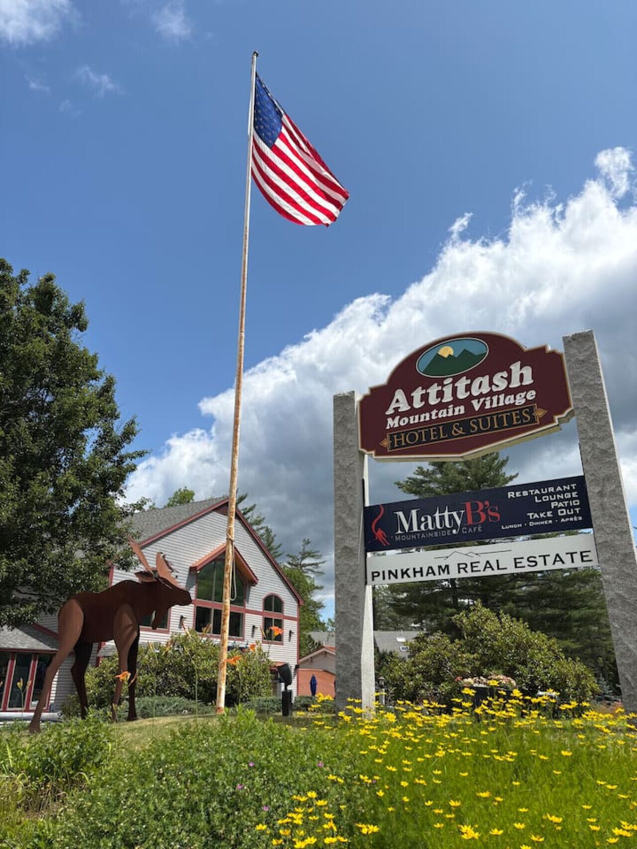 Une enseigne pour l’hôtel et les suites Aritash Mountain Village, avec un drapeau, une statue de cheval et un motif représentant une montagne.