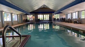 An indoor swimming pool with clear water, a metal ladder, and chairs around the pool. - Attitash Room: Pool, Hot Tub, Storyland, Foliage (Bartlett)