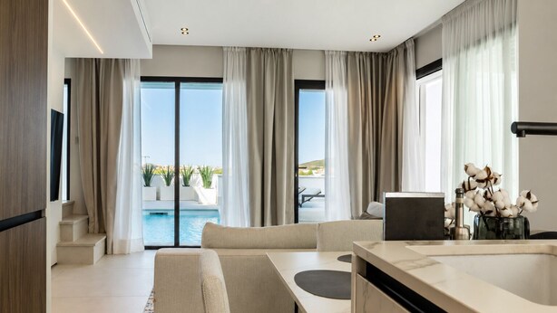 A modern hotel room with a pool view, a sofa, a dining table, and a kitchen area.