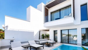 A modern outdoor pool area with lounge chairs and a view of the sea.