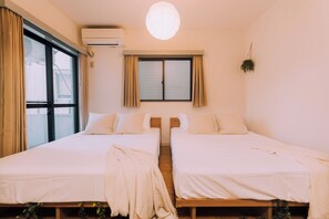 A room with two beds, a window with curtains, an air conditioning unit, and a hanging plant. - Showa Bloom · Stay Near Shinjuku & Yoyogi (Tokyo)