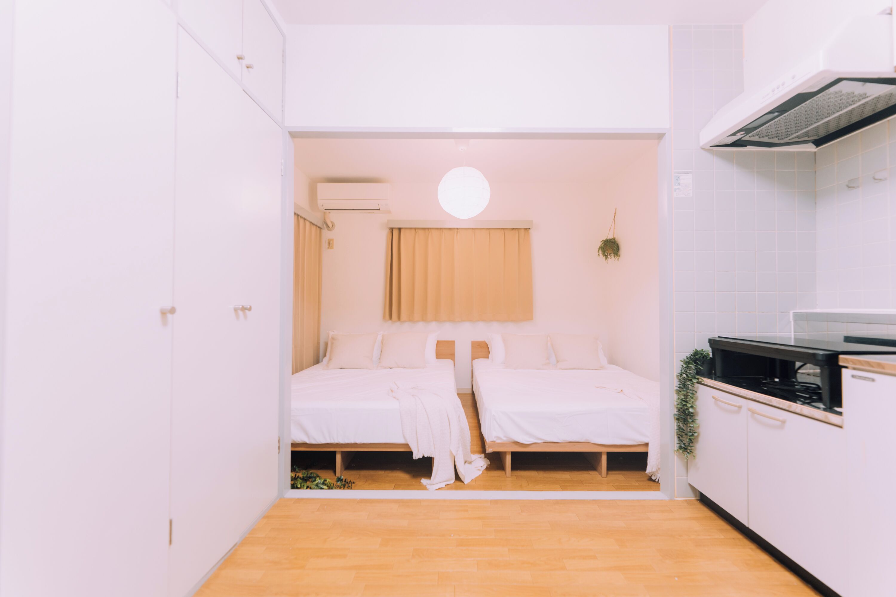 A compact bedroom with two beds, a small kitchenette, and a ceiling light.