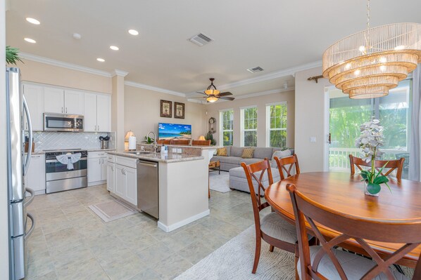 A modern kitchen with white cabinets, a central island, and a dining area with a wooden table and chairs.