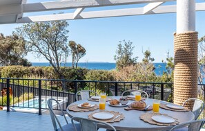 A table set for breakfast with a view of the sea, a rope-wrapped column, and a pool in the background. - Myth On Mollymook Mountain - Bannister Pt - Spa & Games Room (Mollymook Beach)