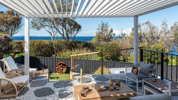 A covered outdoor patio with seating, a table with food and drinks, and a view of the sea.